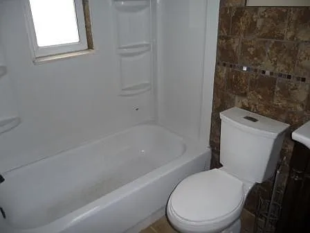Full sized bathtub and shelved white shower surround with privacy window. Modern push button white toilet.