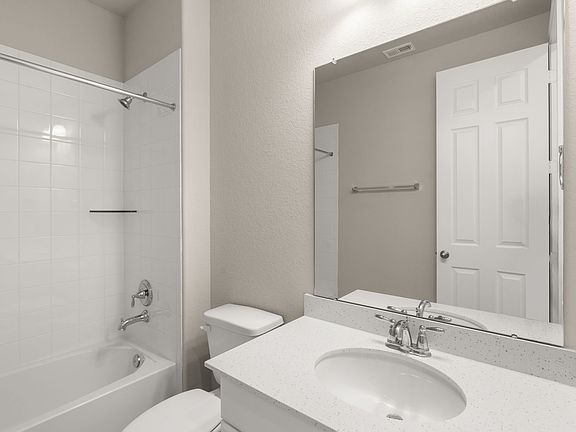 The private bath features tile flooring, white cabinetry with light countertops and a shower tub com