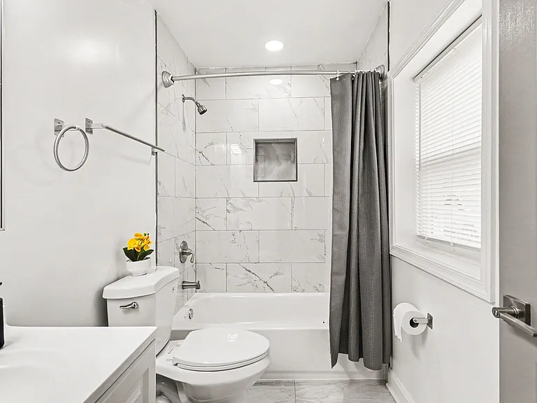 Full bathroom with tiled tub/shower surround, built-in niche, and a window with blinds for light and ventilation.