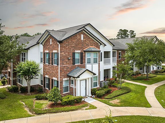 Charming two-story brick apartment building with manicured gardens and winding walkways under a serene sky.