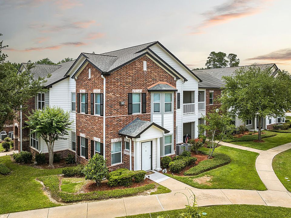 Charming two-story brick apartment building with manicured gardens and winding walkways under a serene sky.