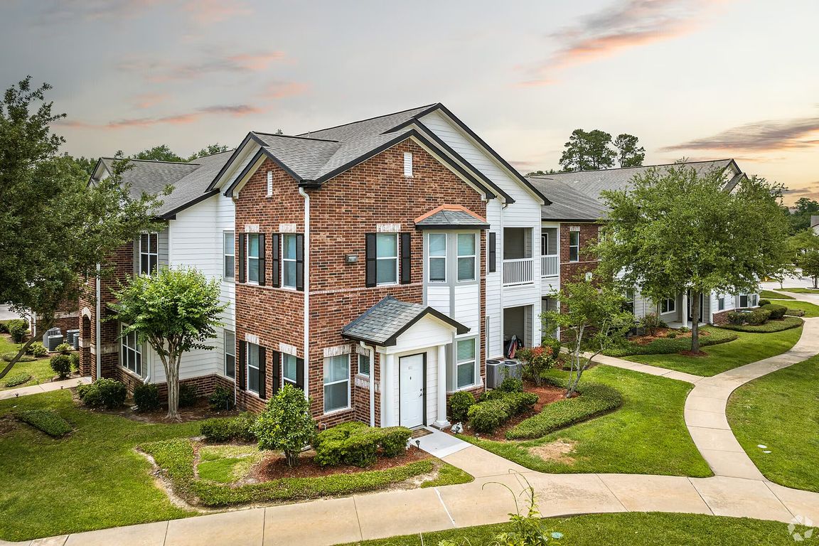 Charming two-story brick apartment building with manicured gardens and winding walkways under a serene sky.