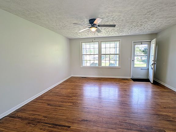 The living room looking from the kitchen and dining room area to the front of the house. Large windows allow for plenty of natural light. Fresh paint, beautiful hardwood floors and ceiling fan make this common space open and inviting.