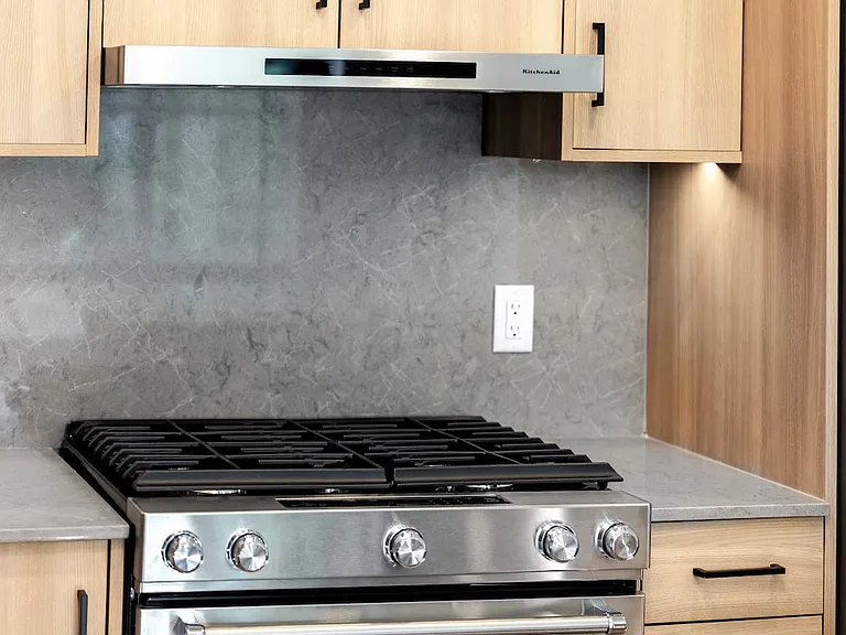 Signature Collection kitchen with stainless steel appliances, quartz countertops, and quartz tile backsplash