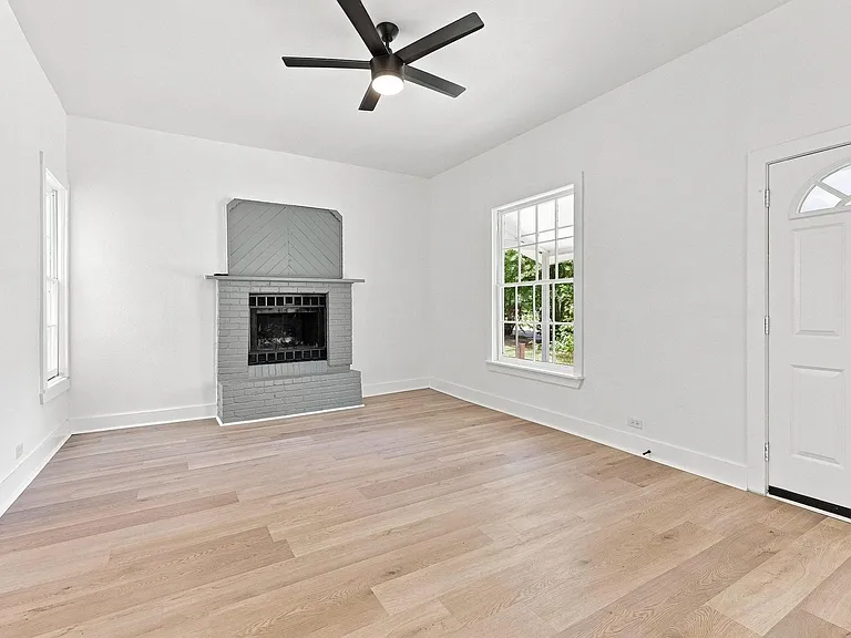 Spacious living area featuring wood-finish flooring, a contemporary ceiling fan, and a fireplace with a gray brick surround