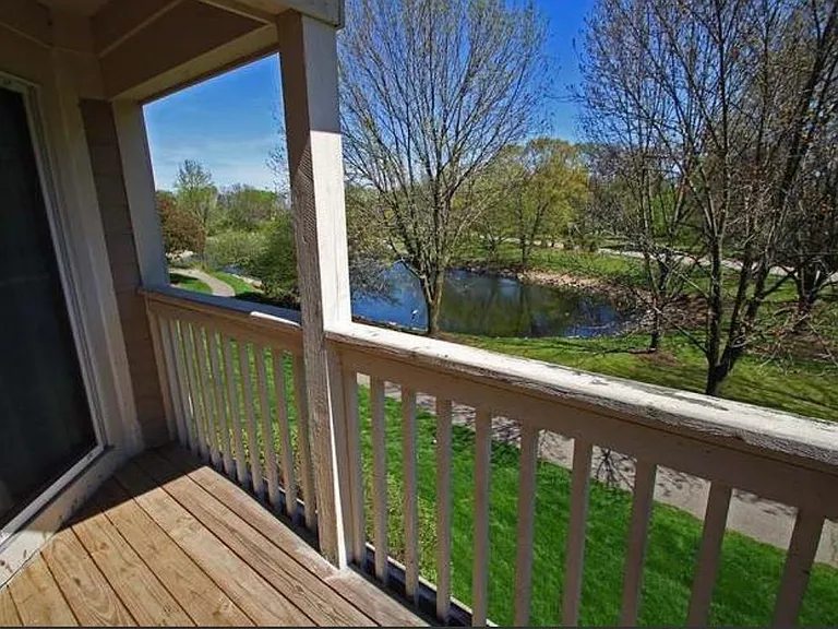 Sliding glass double doors lead to a private balcony overlooking a beautiful lake, open green space, and walking paths.