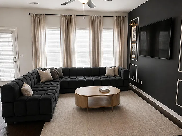 Well-appointed living room with sectional seating, large windows with curtains, ceiling fan, and a mounted TV feature wall.