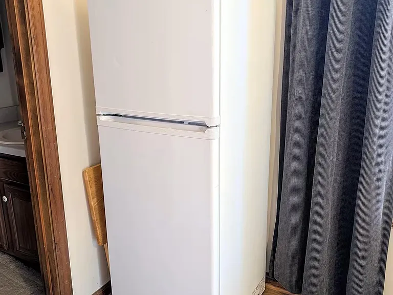 Full-size refrigerator provides convenient food storage for residents, placed on easy-to-clean wood flooring.