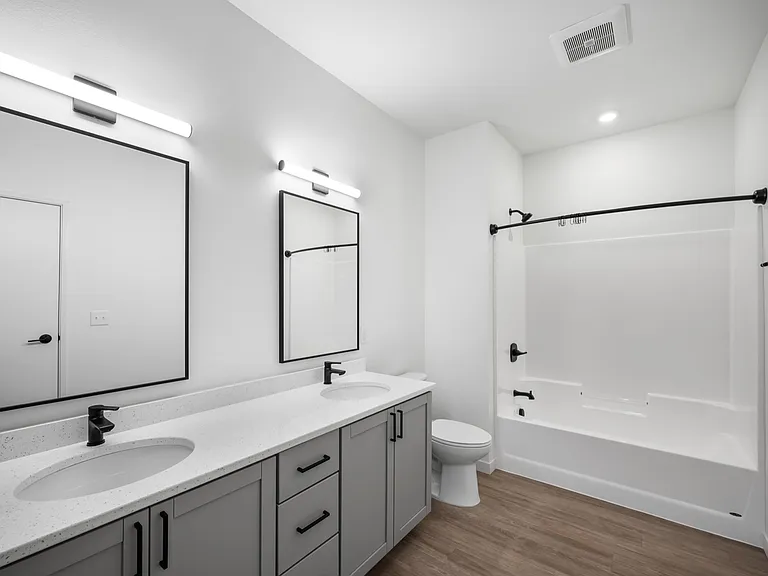 Elegant bathroom featuring a dual sink vanity with modern fixtures, sleek mirrors, and a pristine bathtub, highlighted by stylish lighting and wood flooring. Elegant bathroom featuring a dual sink vanity with modern fixtures, sleek mirrors, and a pristine
