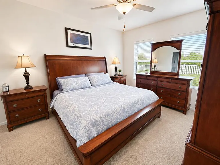 Spacious bedroom with a full bed set, matching dressers, and dual windows with blinds for natural light and privacy.