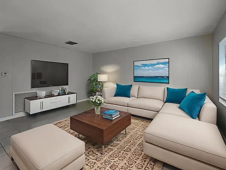 Modern living room featuring plush beige sectional sofa with vibrant teal cushions, chic wooden coffee table, wall-mounted TV, and large window for natural light.