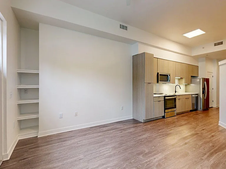 Apartment Kitchen with Stainless Steel Appliances, Dining and Living Room with Wood Style Flooring.