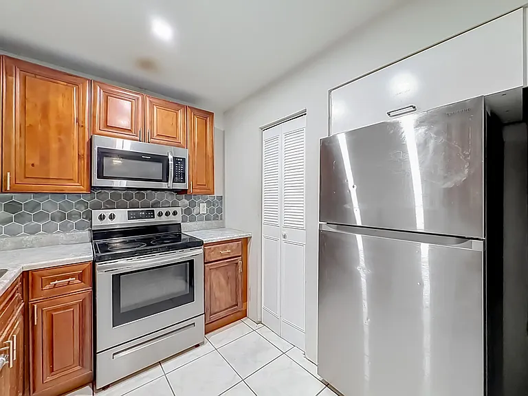 Efficient kitchen with stainless steel appliances, ample wood cabinetry, and a tile backsplash plus nearby pantry storage.