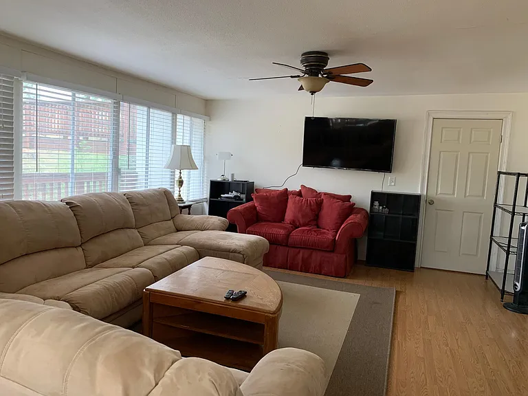 another view of living room with ceiling fan, wall of windows and bathroom access