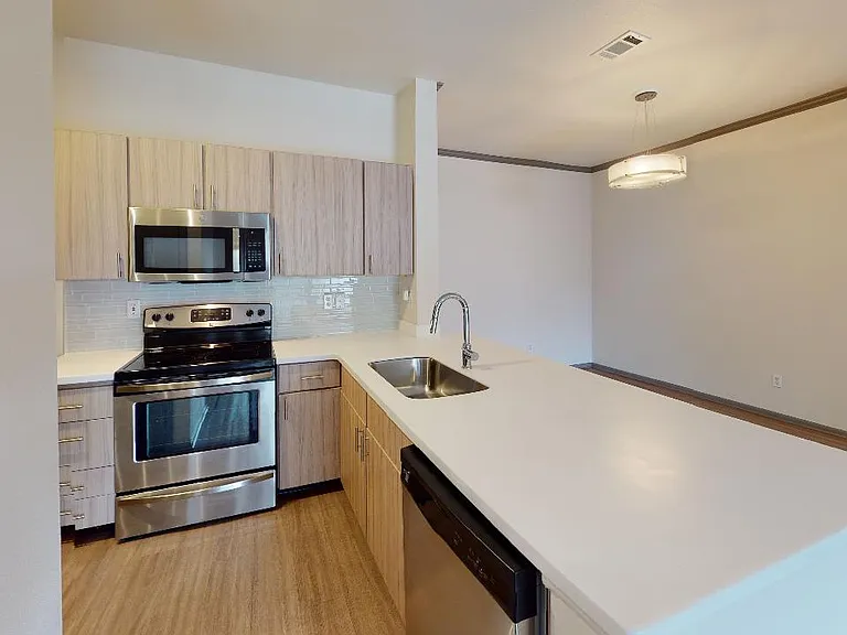 Apartment kitchen with stainless steel appliances, quartz countertops and wood-style flooring.