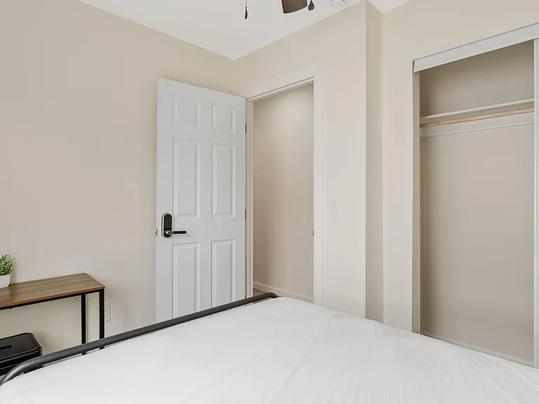 Private bedroom featuring a secure entry door, open closet with hanging rod and shelf, and space for a bed and desk.