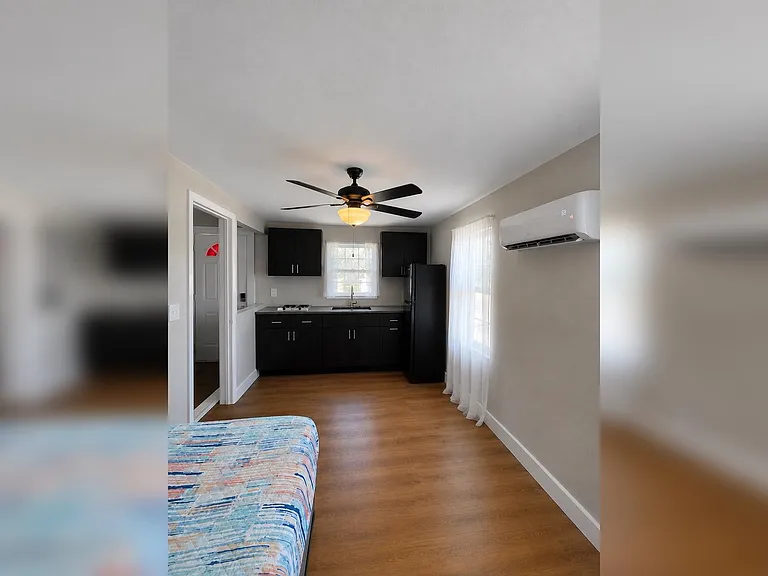 Open-concept studio with kitchenette, ample cabinet storage, and a windowed sink area plus mini-split A/C for comfort.