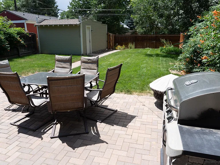 Back patio with table and chairs, BBQ grill and fire pit. The view is looking West with the one car garage far left.