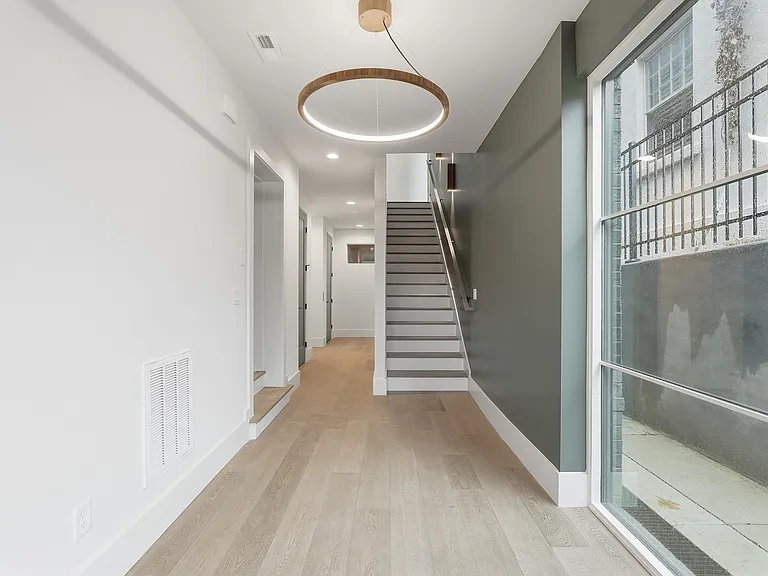 Bright, modern entryway featuring wide plank flooring, statement lighting and a sleek staircase design.