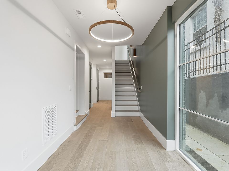 Bright, modern entryway featuring wide plank flooring, statement lighting and a sleek staircase design.