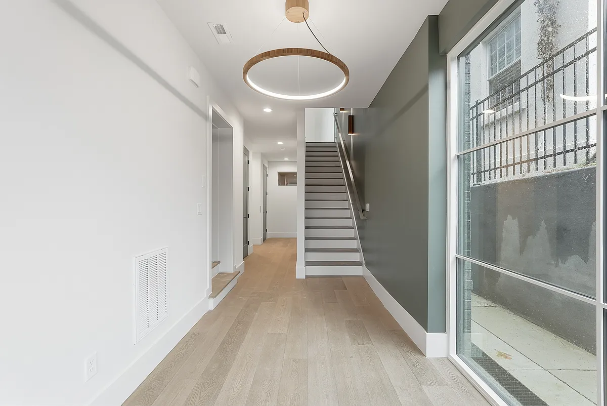 Bright, modern entryway featuring wide plank flooring, statement lighting and a sleek staircase design. - 3718 W End Ave #1