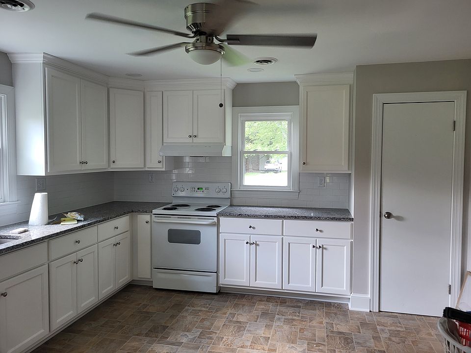 Kitchen view from utility room door featuring white custom cabinets with granite counter tops, tile backsplashes, electric stove and pantry closet