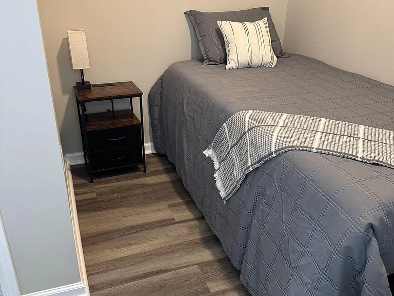 Furnished bedroom with a full-size bed, nightstand with lamp, and durable wood-look flooring for easy upkeep.