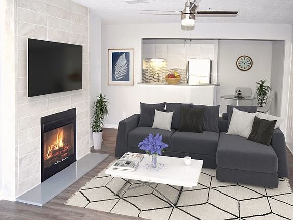 Modern living room with fireplace, ceiling fan with light and partial view of the kitchen