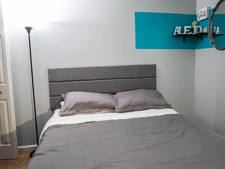Furnished bedroom with a full-size bed, padded headboard, and bedside floor lamp.