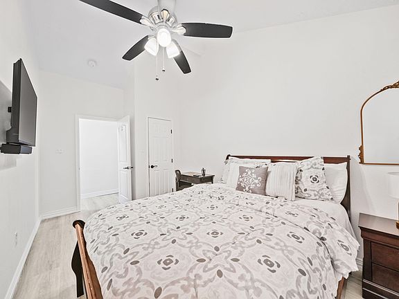 Furnished bedroom with a full bed, nightstands, dresser, ceiling fan, and wall-mounted TV for comfortable daily living.