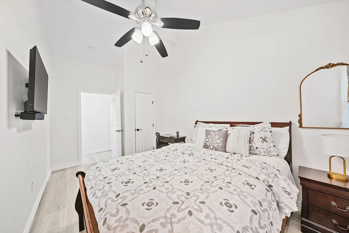 Furnished bedroom with a full bed, nightstands, dresser, ceiling fan, and wall-mounted TV for comfortable daily living. - Bouldgreen St