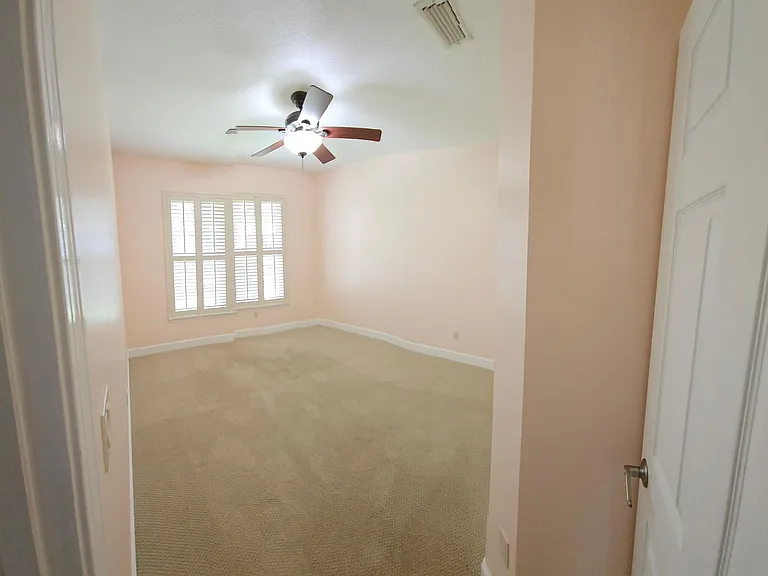 Bedroom 3, painted in light salmon, with wood shutters, closet, and ceiling fan.