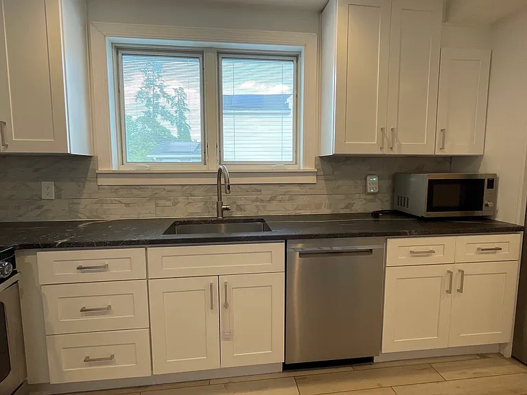 Bright kitchen sink area with ample cabinet storage, dishwasher, stainless steel appliances, and a window for natural light.