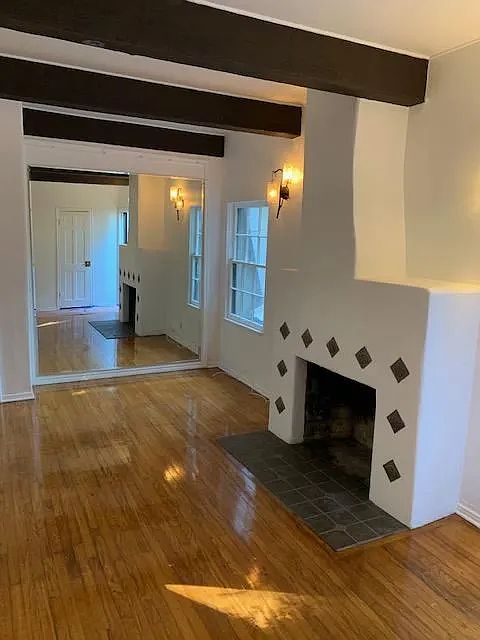 Wonderful living room with a full mirrored wall, dramatic wood, beam ceiling, attractive fireplace, and attractive, hardwood floors, all for your delight and pleasure.