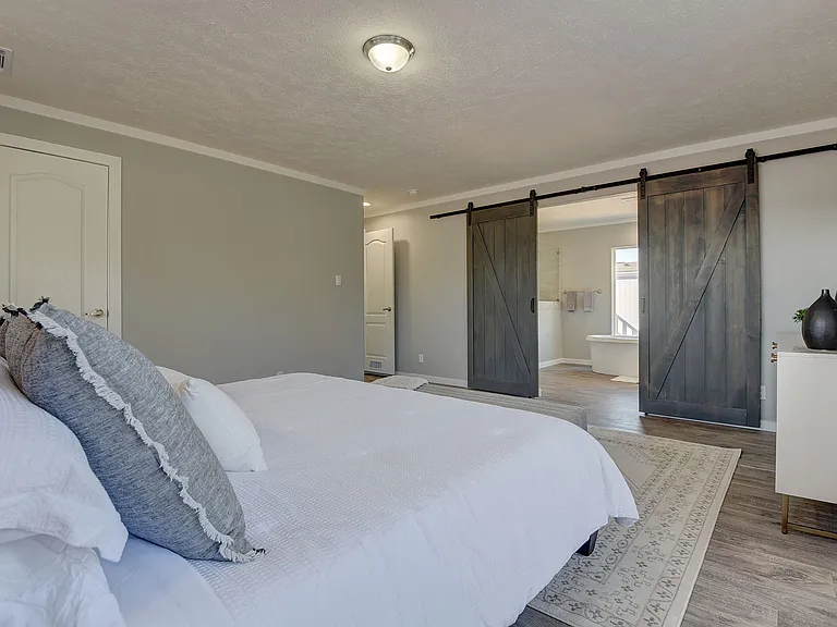 Spacious primary suite with rustic sliding barn doors opening to a spa-like bath_blending modern comfort with upscale, designer touches.