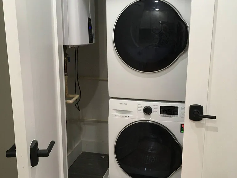 Tankless hot water heater on wall to the left. Stackable full-sized washer and dryer to the right.