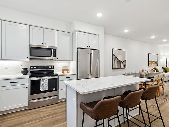 A modern, open-concept kitchen with white cabinets, stainless steel appliances, and a large central