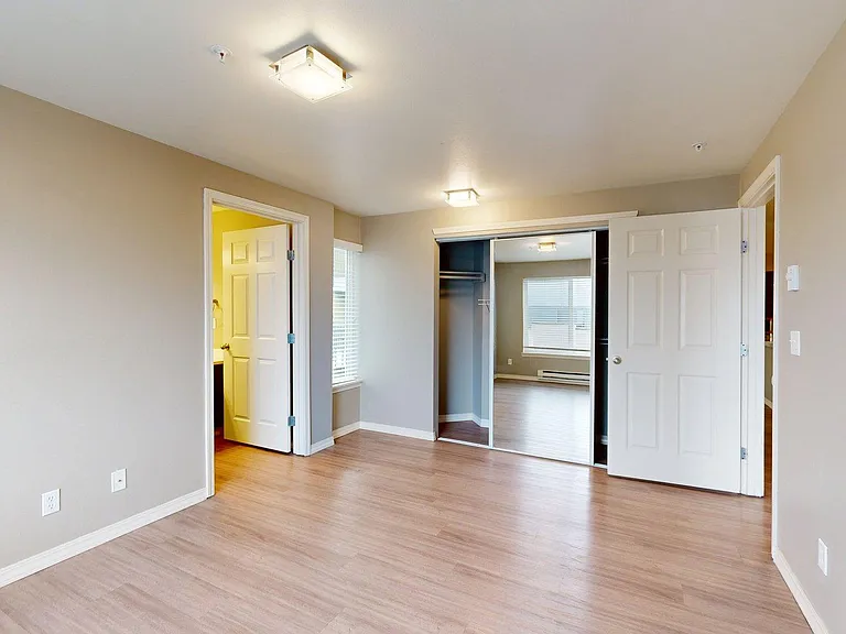 Spacious apartment bedroom with attached bathroom and wood-style flooring.