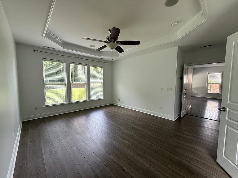 Primary bedroom retreat featuring an elegant double-tray ceiling with crown molding, a central ceiling fan, and premium wide-plank flooring looking out to the expansive backyard