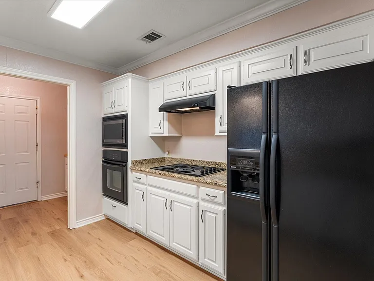 Kitchen featuring wood-finish flooring, white cabinetry with silver hardware, granite-style countertops, and black built-in appliances