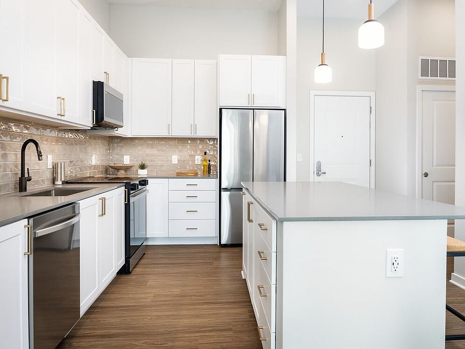Design Collection I kitchen with white cabinetry, beige tile backsplash, grey quartz countertops, pendant lighting and hard surface flooring