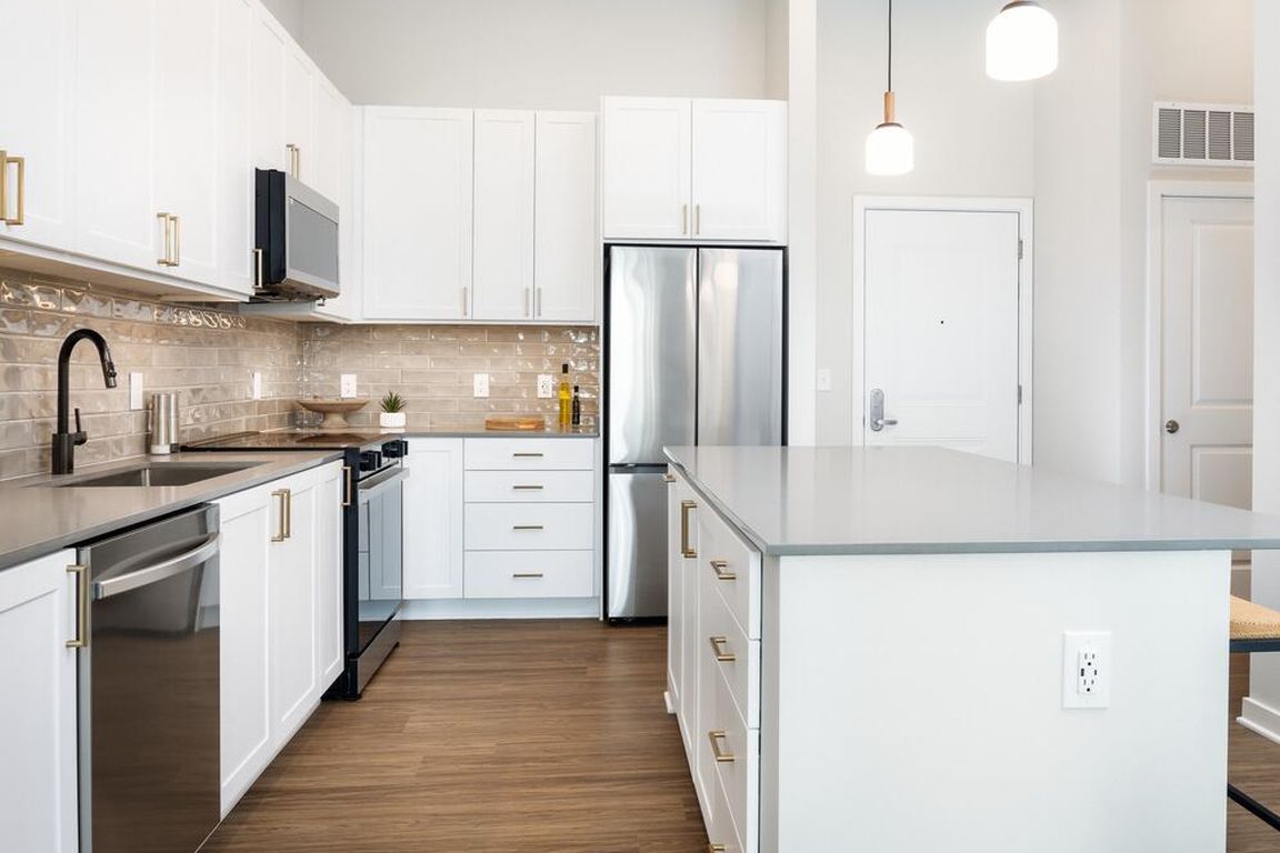 Design Collection I kitchen with white cabinetry, beige tile backsplash, grey quartz countertops, pendant lighting and hard surface flooring