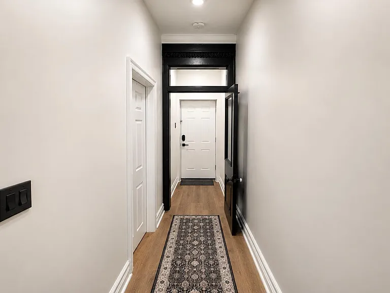 Long entry hallway with hardwood-style flooring, overhead lighting, and access to multiple rooms near the front door.