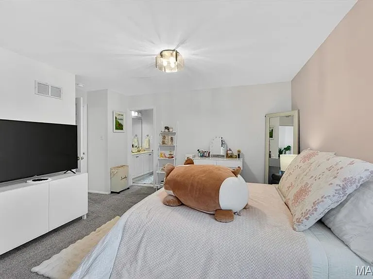 Carpeted interior space featuring white walls and a contrasting accent wall, a flush-mount ceiling light fixture, and an open doorway revealing a vanity with built-in cabinetry