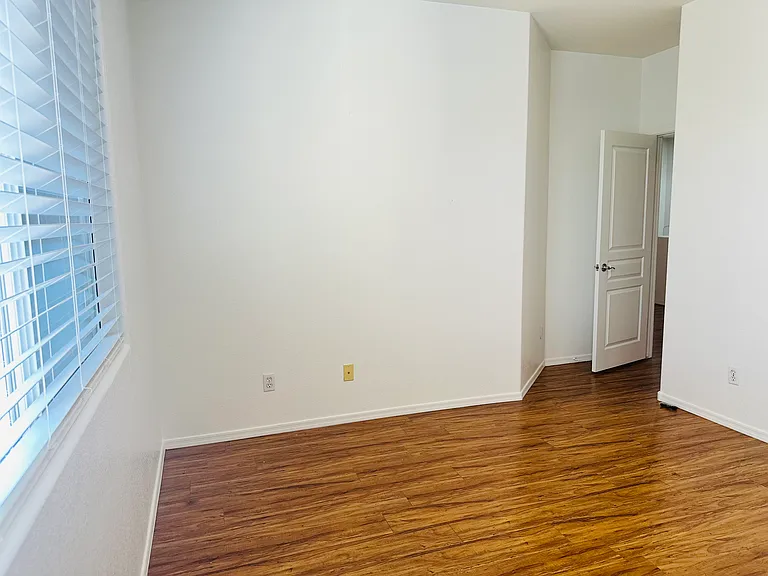South-facing upstairs bedroom overlooking the backyard and private pool, with abundant natural light and wood-look flooring.