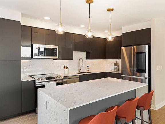 Renovated Package I kitchen with grey cabinetry, white marbled quartz countertops and backsplash, stainless steel appliances, and hard surface flooring
