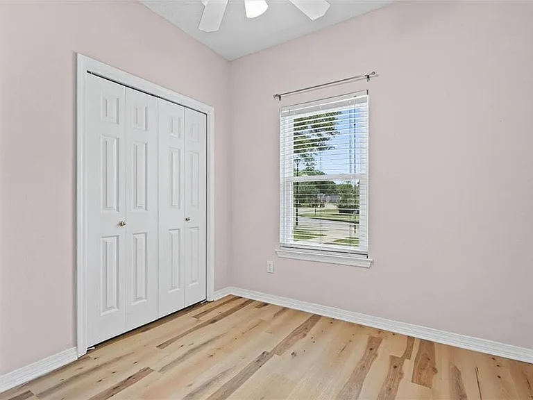 Room featuring wood-finish flooring, a double bi-fold closet, a single window with blinds, and a ceiling fan