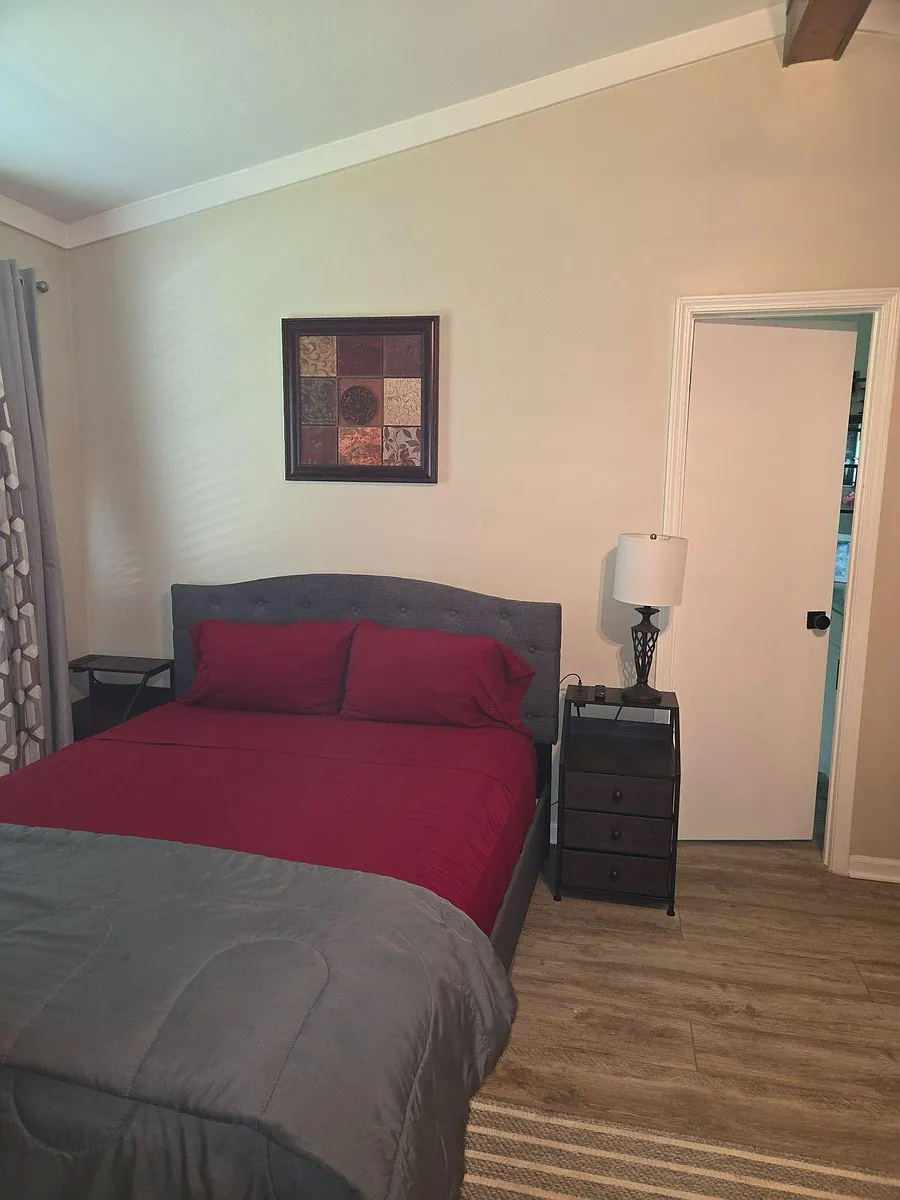 Furnished bedroom with a full bed, nightstands, and lamp, plus easy access to the adjacent hall/bath area. - S Narrow Oak Ln