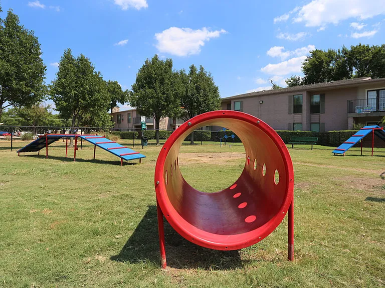 Spacious on-site dog park with open green space and agility equipment, perfect for pets to run, play, and socialize in a fenced, pet-friendly environment.