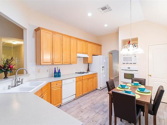 This spacious kitchen features high ceilings, wood cabinets, light countertops, matching appliances, modern tile backsplash, recessed lighting, and lovely breakfast area!
